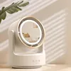 A white desk fan with a built-in LED mirror and gold trim sits on a wooden surface, with a plant and shadows in the background. Produktbild-Vorschau