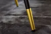 Close-up of the gold and black leg of a chair resting on a dark, textured rug. Produktbild-Vorschau