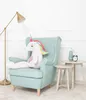 A plush unicorn toy sits on a chair next to small tables with decorative items. Podgląd zdjęcia produktu