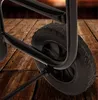 A close-up view of a black metal cart wheel and frame resting on a wooden floor. Anteprima dell’immagine prodotto
