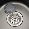 A close-up view of a stainless steel sink drain with a removable strainer basket and a gray lid. Podgląd zdjęcia produktu