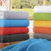 Stacks of colorful towels are arranged on a wooden surface in front of a window with greenery visible outside. Produktbild-Vorschau