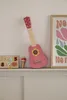A pink toy guitar with a flower design sits on a shelf next to a number puzzle and a maraca. Produktbild-Vorschau