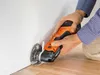 A person is using an oscillating multi-tool to cut near a wall and floor. Náhľad obrázku produktu