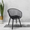 A black chair sits on a rug in front of a textured wall, with a potted plant to the left. Produktbild-Vorschau