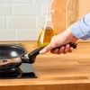 A hand holding a frying pan over a stovetop. Produktbild-Vorschau