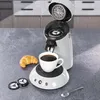 A coffee machine with a cup of coffee and a croissant on a countertop. Produktbild-Vorschau