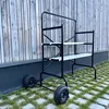 A black metal rolling scaffold with two levels is shown outdoors against a wooden wall. Anteprima dell’immagine prodotto