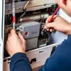 A technician is working on the internal components of a furnace or boiler, using a digital thermostat regulator. Produktbild-Vorschau