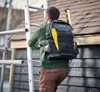 A man wearing a tool backpack climbs a ladder next to a wooden structure with a shingled roof. Voir les images du produit