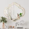 A decorative mirror with a gold frame is mounted on a white wall above a console table. The table displays various decorative items, including a vase with branches, a ceramic jar, a green plant, and a silver horse sculpture. Produktbild-Vorschau