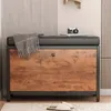A shoe cabinet with a cushioned seat, a blanket draped over it, and a camera and book on top. Slippers are on the floor in front. Podgląd zdjęcia produktu