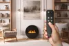 A hand holding a remote control in a modern living room with a fireplace. Náhled obrázku produktu