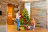 A woman and a child are decorating a Christmas tree in a room with wooden walls. Produktbild-Vorschau