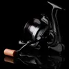 A black fishing reel with a wooden handle is shown against a black background, with its reflection visible below. Produktbild-Vorschau