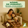 A mother and daughter are cuddling on a couch under a blanket, reading a book. Produktbild-Vorschau