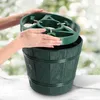 Hands are shown placing a green Christmas tree stand into a green barrel-shaped planter. Voir les images du produit