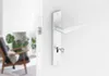 A white door handle with a key inserted into the lock, set against a white wall. In the blurred background, a chair and plants are visible. Produktbild-Vorschau