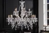 A crystal chandelier hangs in a dimly lit room with a black wall and a window showing a city skyline at night. Náhled obrázku produktu