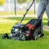 A person is using a Scheppach lawnmower to cut grass in a yard. Produktbild-Vorschau