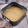 A square baking pan filled with cake batter, sitting on a wooden surface with eggshells nearby. Podgląd zdjęcia produktu
