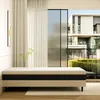 A mattress is displayed in a modern room with large windows overlooking a building and greenery. Voir les images du produit