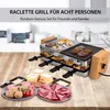 A raclette grill is set up on a wooden table with various food items like meat, cheese, and potatoes arranged around it. The grill has food cooking on its top surfaces and in the lower trays. Produktbild-Vorschau