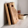 Two wooden cutting boards are leaning against a white wall, with a basket of bread and a bottle of drink in the background. Náhľad obrázku produktu