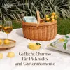 A picnic setup on a white blanket outdoors, featuring a wicker basket filled with lemons and a book, two glasses of beverage, and a lemon-patterned pillow. Produktbild-Vorschau