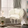 A cozy indoor corner with a hanging chair, a side table with a lamp and plant, and a rug. Podgląd zdjęcia produktu