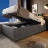 A storage bed with its mattress lifted to reveal the storage compartment. It is placed in a room with a window and a wall with vertical wooden slats. Voir les images du produit