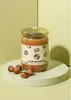 A jar of hazelnut spread is placed on a light green pedestal, with hazelnuts scattered around it. Produktbild-Vorschau