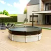 A round pool cover is shown on a wooden deck next to a modern house and garden furniture. Produktbild-Vorschau