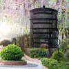 A black drying net with multiple shelves hangs outdoors, surrounded by lush greenery and blooming wisteria. Produktbild-Vorschau