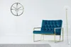 A modern living room with a teal armchair, a gold-framed wall clock, and a tall vase with a white flower. Náhled obrázku produktu