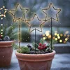 Three illuminated star garden stakes are planted in a terracotta pot filled with soil, pine branches, pinecones, and red berries, set against a snowy, bokeh background. Náhľad obrázku produktu