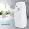 A white automatic air freshener dispenser is shown in a clean, modern room with large windows overlooking a garden. Produktbild-Vorschau