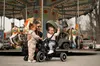 A woman and two young children are at a carousel. Produktbild-Vorschau