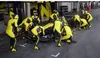 A Formula 1 pit crew in yellow and black uniforms working on a race car during a pit stop. Produktbild-Vorschau
