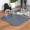 Two clear glasses are placed upside down on a gray drying mat in front of a sink. Produktbild-Vorschau