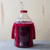 A clear plastic carboy filled with dark purple liquid, adorned with red ribbon, set against a light wooden background. Produktbild-Vorschau