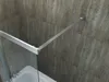 Close-up of a shower enclosure corner with a metal frame and glass panel, mounted on a tiled wall above a bathtub. Produktbild-Vorschau