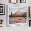 A Samsung Frame TV displaying a landscape image is mounted on a wall alongside other framed pictures. Produktbild-Vorschau