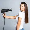 A woman is holding a black hairdryer. Produktbild-Vorschau