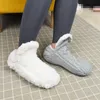 Person, die eine weiße flauschige Hausschuh-Socke und eine graue gestrickte Hausschuh-Socke auf einer karierten Matte trägt Náhľad obrázku produktu