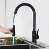A person is using a black pull-down kitchen faucet to rinse vegetables in a sink. Produktbild-Vorschau