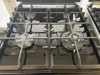 A close-up view of a black gas stove top with four burners and metal grates. Produktbild-Vorschau