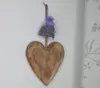 A wooden heart decoration with a small lavender sachet hanging from it, displayed on a textured white wall next to a patterned curtain. Produktbild-Vorschau