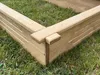 A close-up view of the corner of a wooden raised garden bed, resting on grass. Produktbild-Vorschau