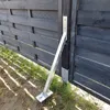 A metal ground anchor is attached to a wooden fence post. Produktbild-Vorschau